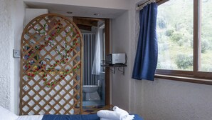 A hotel room with a bed, a wooden decorative partition, a window with curtains, and a view of greenery outside. - Apartment in a studio villa called Salina 3 beds (REITANO)