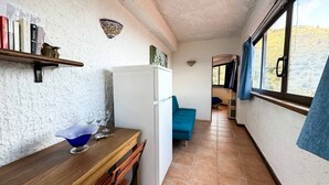 A narrow hallway with a wooden table, a blue chair, a white refrigerator, and a window with a view of a hilly landscape. - Apartment in a studio villa called Salina 3 beds (REITANO)