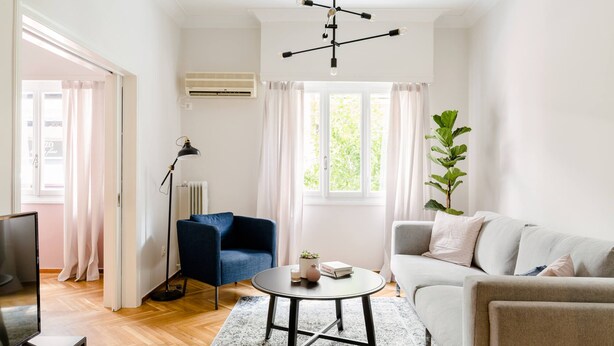 A modern living room with a sofa, a blue armchair, a round coffee table, a floor lamp, and a potted plant. - Acropolis Heart 2BD Apartment in Plaka (Athens)