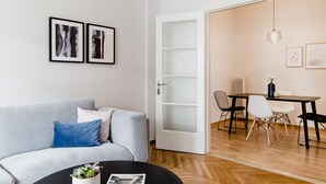 A modern living room with a grey sofa, a coffee table with a plant, and a dining area with a table and chairs. - Acropolis Heart 2BD Apartment in Plaka (Athens)