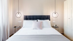 A neatly made bed with white linens and a dark headboard, two bedside tables with lamps, and a white wardrobe. - Acropolis Heart 2BD Apartment in Plaka (Athens)