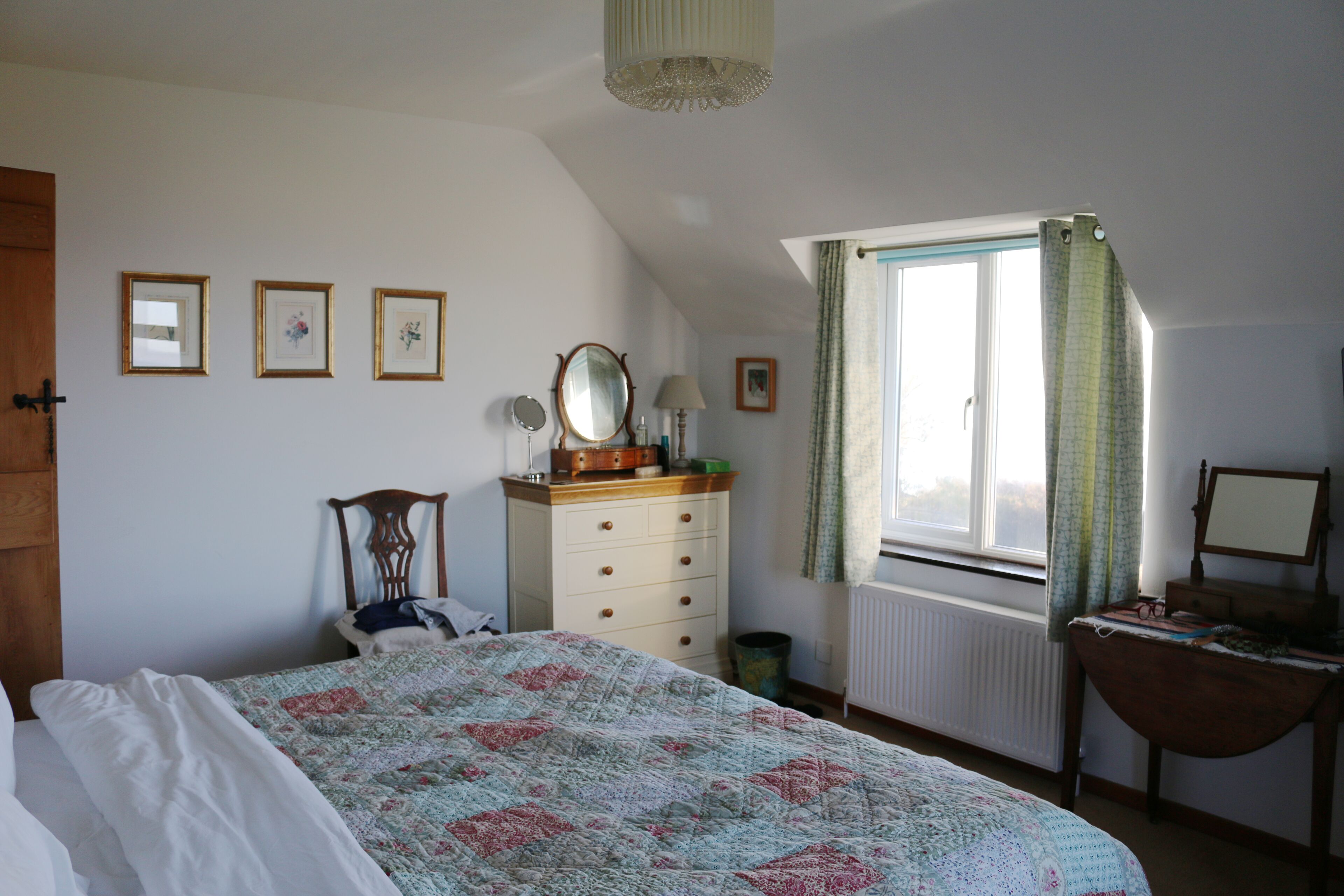 A bedroom with a bed, dresser, mirror, and window with curtains.