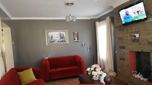 Uma sala de estar com um sofá vermelho, uma poltrona listrada, uma mesinha com um vaso e uma lareira.