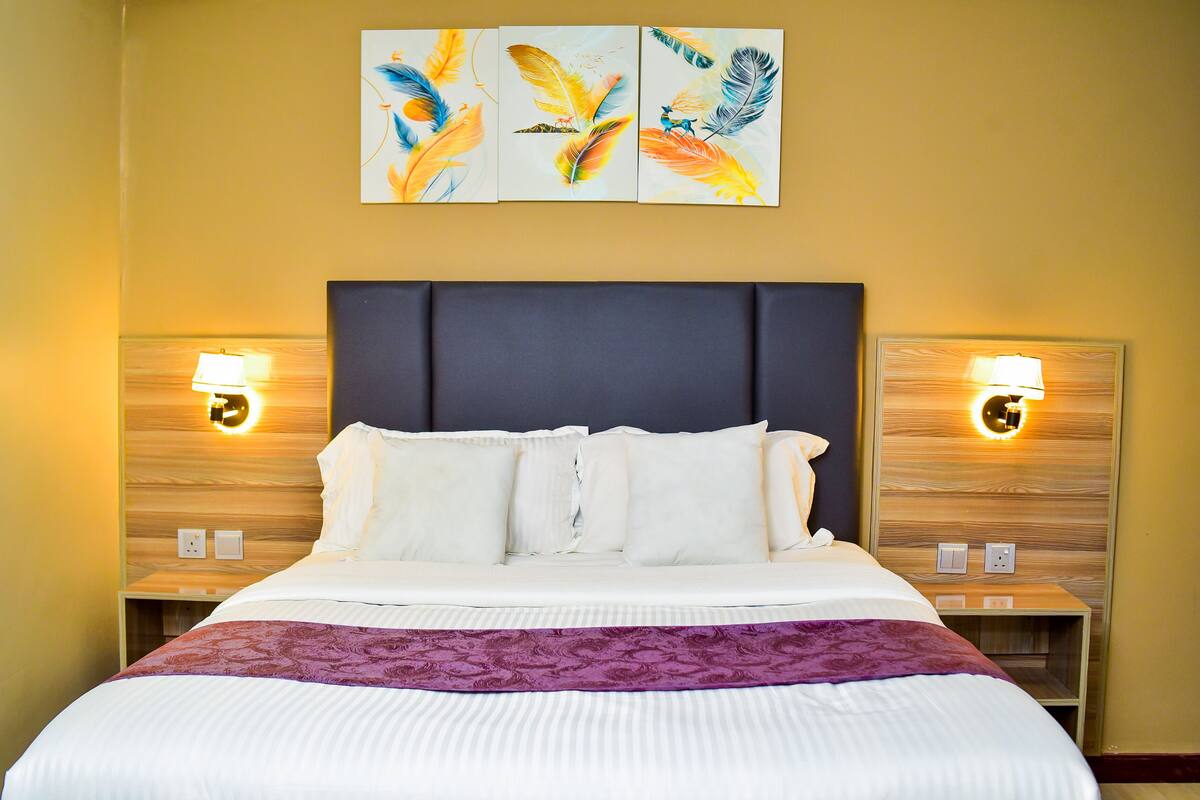 A hotel room with a large bed, two bedside tables, a headboard, and wall-mounted lamps.