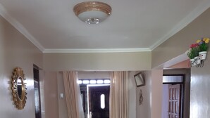 Um corredor com piso de madeira, luminária no teto, porta com cortinas e uma lixeira.