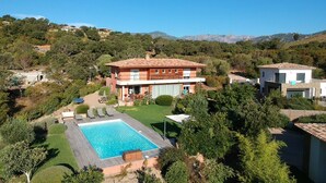 Ein zweistöckiges Haus mit Swimmingpool, umgeben von Grünflächen und Hügeln.