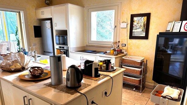 Una cocina moderna con armarios blancos, horno empotrado, cafetera y hervidor sobre la encimera.