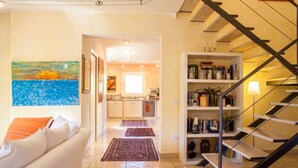 Una sala de estar moderna con sofá, un cuadro, una escalera y una cocina al fondo.