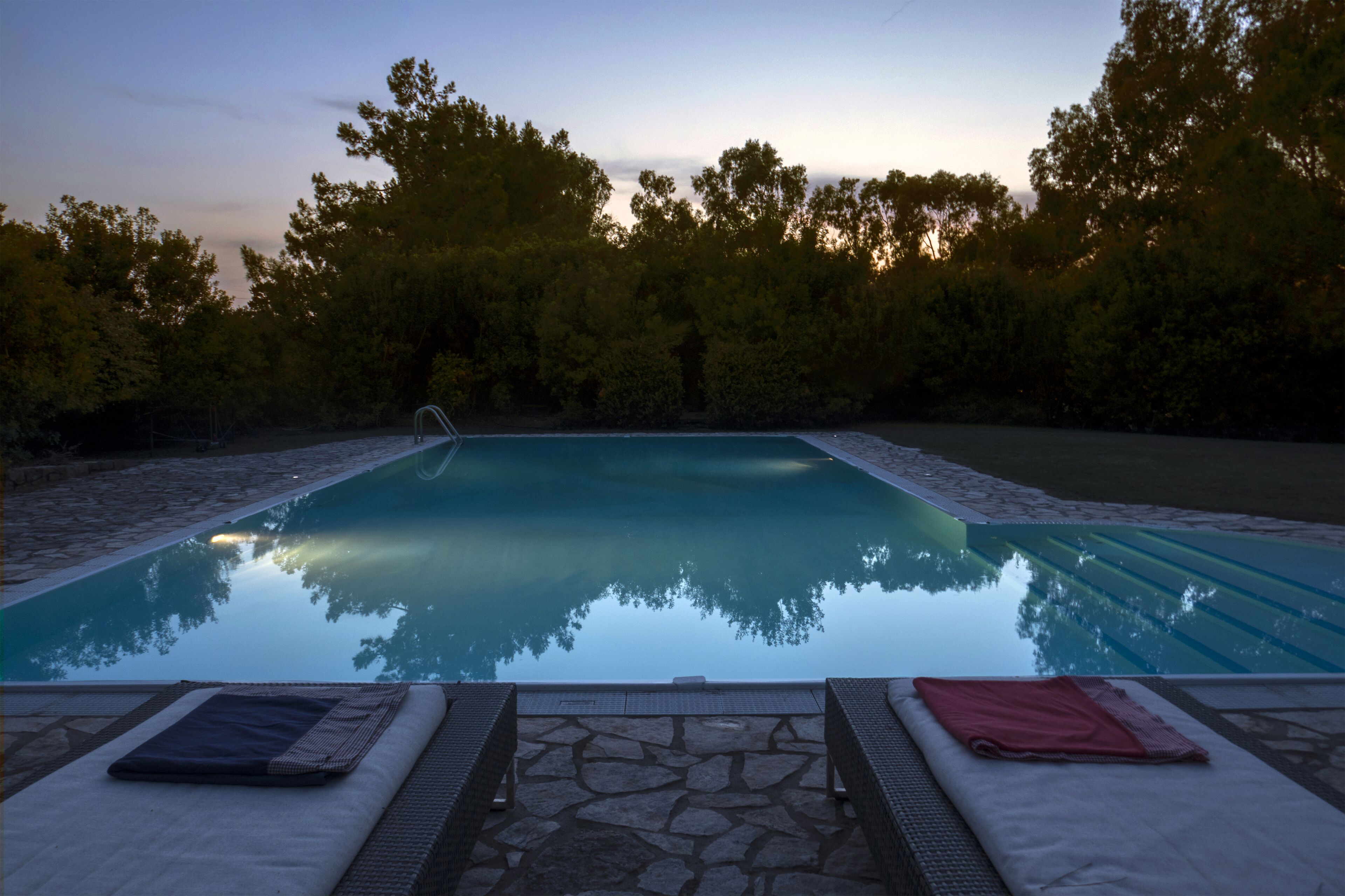 A swimming pool with a stone border and lounge chairs with towels.