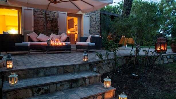 Un patio de piedra con mobiliario exterior, faroles y vistas al interior.