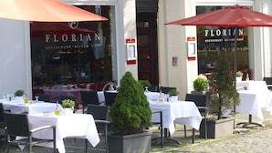 An outdoor seating area with tables and chairs, potted plants, and umbrellas at a restaurant named 'FLORIAN'. - Messewohnung Gräfrath (Solingen)