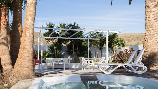Een zwembadgedeelte met een witte pergola, lounge fauteuils en een bank.
