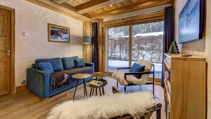 Una habitación acogedora con un sofá azul, una mesita redonda pequeña, un tapete blanco mullido y un mueble de televisión de madera.