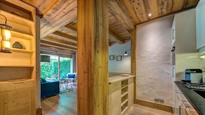 Interior de madera con área de cocina, vigas de madera y vista a la vegetación exterior.