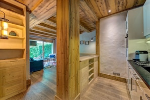 A wooden interior with a kitchen area, wooden beams, and a view of greenery outside.