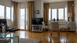 Un salon moderne doté d’un téléviseur à écran plat, d’une table basse en verre, d’un canapé et d’un coin repas avec des chaises et une table.