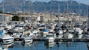Un port de plaisance où sont amarrés de nombreux bateaux, entouré de bâtiments et avec des montagnes en arrière-plan.