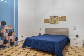 A bedroom with a bed, a nightstand, a dresser, and a wall with hexagonal tiles and artwork.
