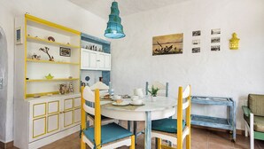 Uma área de refeições com uma mesa branca, cadeiras amarelas e um luminária pendente azul.