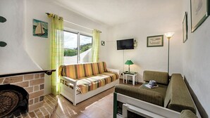 Uma sala de estar acolhedora com um sofá, um pufe, uma televisão de tela plana e uma lareira.