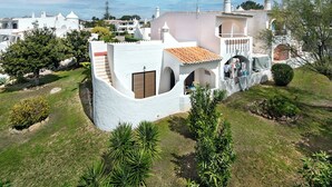 Uma vila branca com telhado de cerâmica, rodeada por vegetação e outros edifícios brancos ao fundo.