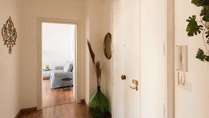 A hallway with a door leading to a room with a bed and a chair. There is a green vase with dried plants on the floor. - Panorama Vesuvius 3 (Central) private room in apartment (Napoli)