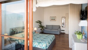 A bedroom with a bed, a sofa, a small table with a lamp, a plant, and a TV on a stand. - Panorama Vesuvius 3 (Central) private room in apartment (Napoli)