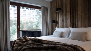 Un dormitorio con una cama grande, un panel de pared de madera, una ventana con cortinas y un radiador.