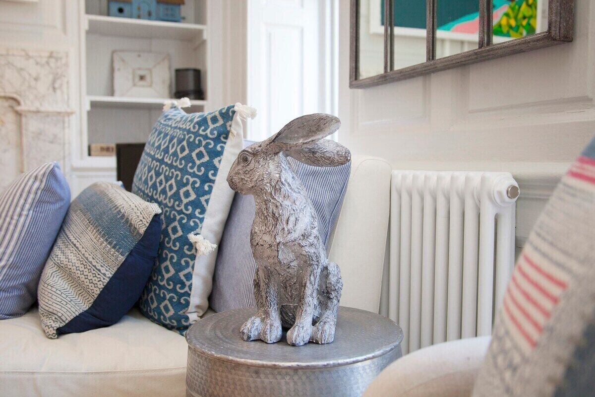 A white sofa with patterned cushions and a silver statue of a rabbit on a round metal table.