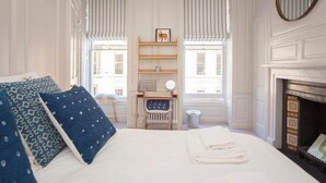 Een slaapkamer met een bed, bureau, stoel, open haard en een raam met uitzicht.