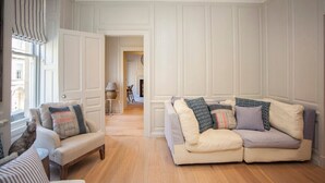 Een woonkamer met een bank en fauteuils, een houten vloer en een deur naar een andere kamer.