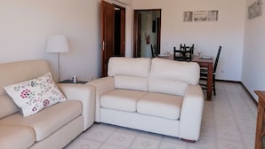 Un salon avec un canapé beige, une petite table avec une lampe et un coin repas comprenant des chaises et une table.