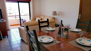 Un coin repas avec une table en bois dressée pour quatre personnes, un canapé et un téléviseur en arrière-plan.