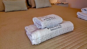 Un lit bien fait, avec une couvre-lit beige et des oreillers, une lampe de chevet et deux serviettes pliées sur lesquelles on peut lire le texte « Formula Holiday Rentals ».