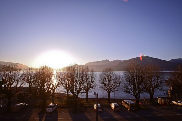 A parking lot with cars and trees, a body of water, and mountains in the background.