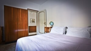 Een slaapkamer met een bed, een houten garderobe, een nachtkastje met een wereldbol en een ingelijste foto aan de muur.