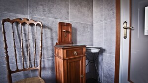 Een badkamer met een houten stoel, een houten kast en een witte wastafel.