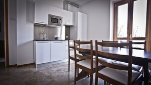 Een moderne keuken met witte kasten, een inbouwmagnetron en een eethoek met houten stoelen en een tafel.