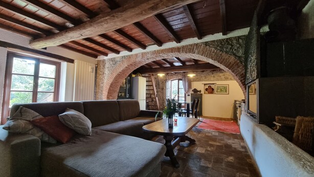 A cozy living room with a wooden ceiling, a stone archway, a sofa, a table, and a fireplace.