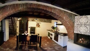 An interior with a brick archway leading to a dining area with a table and chairs, a kitchen with cabinets and a stove, and a decorative wall panel.