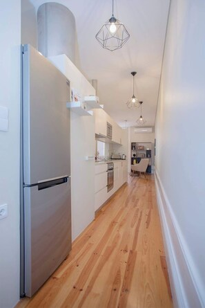 A modern kitchen with a stainless steel refrigerator, wooden flooring, and pendant lighting. - Liiiving In Porto | Bolhão Market Apartment II (Porto)