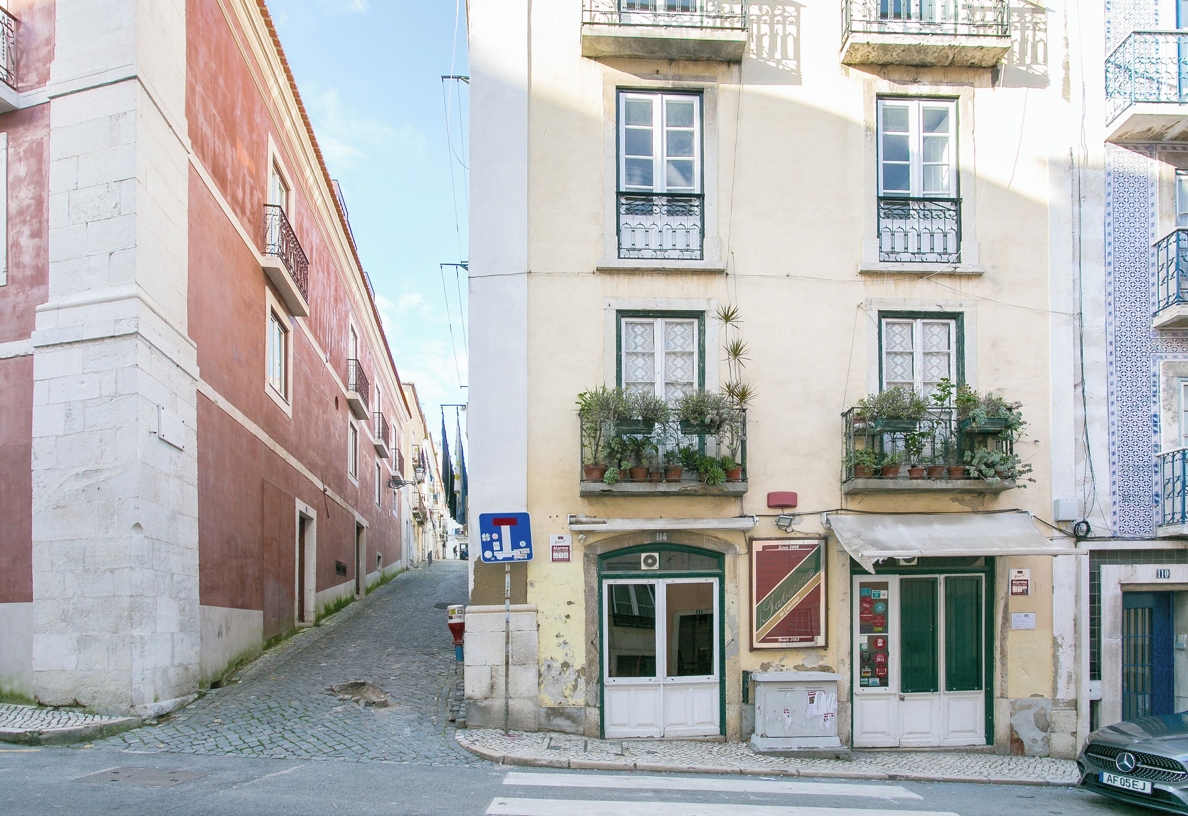 A narrow street with buildings on either side, featuring a shop with a green door and a signboard.