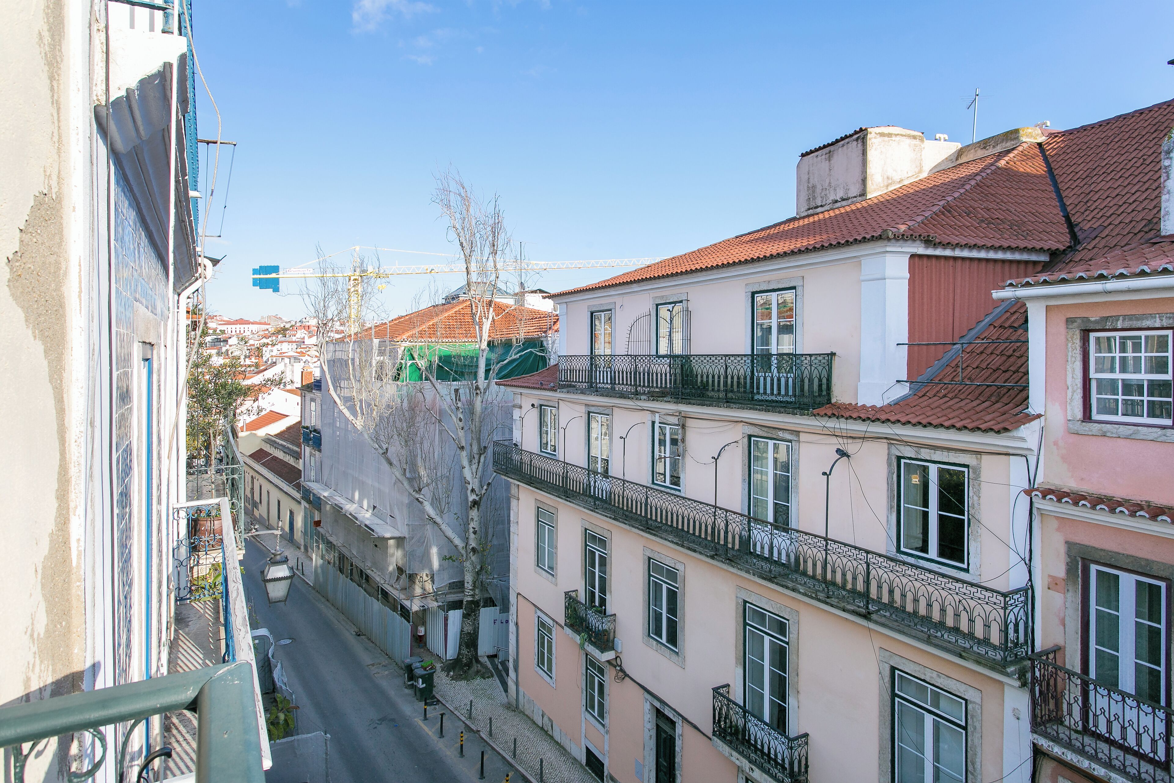 A narrow street with buildings on both sides, featuring balconies and a clear sky.