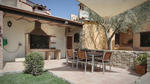 Un patio exterior con pared de piedra, una parrilla y una mesa con sillas.