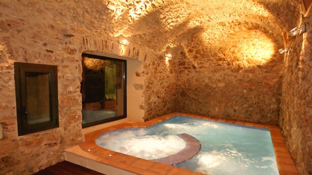 Una habitación con paredes de piedra, una bañera de hidromasaje y suelo de madera.