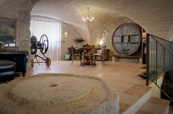 A rustic interior with a stone table, wooden chairs, a chandelier, and a staircase with a metal railing. - Rural house with pool and jacuzzi (Albera, Can Llobet) (Capmany)