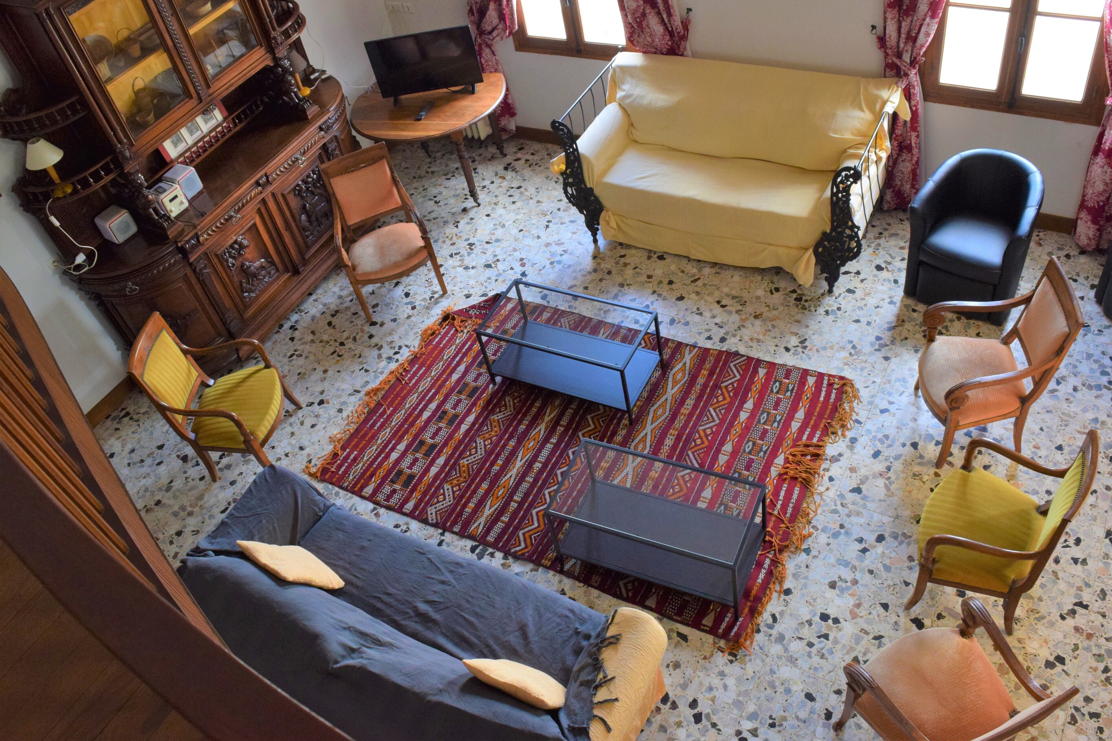 A living room with a sofa, chairs, a TV, a wooden cabinet, and a patterned rug.