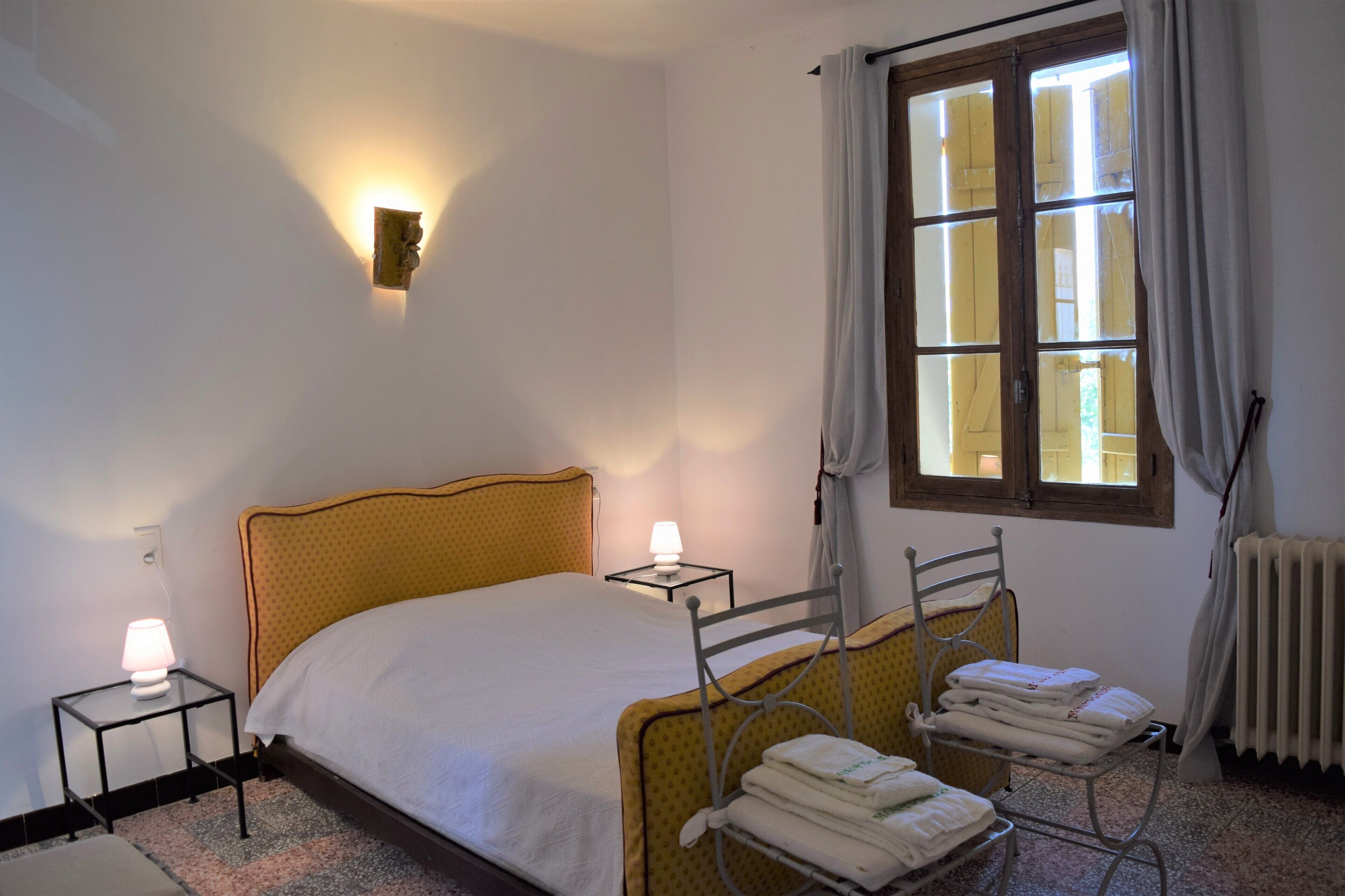 Ein ordentlich eingerichtetes Hotelzimmer mit Bett, Nachttischlampen, Heizkörper und einem mit Vorhängen versehenen Fenster.