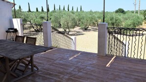 Une terrasse extérieure avec une table et des chaises en bois, entourée d’une clôture en métal.