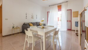 A dining area with a white table and chairs, a sofa, a hanging light fixture, and a window with curtains. - Holiday house in Torre Lapillo beach (TL23) (Torre Lapillo)
